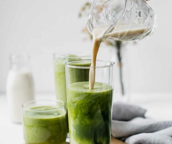 A hand pouring milk into a matcha latte.