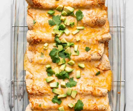 Top shot of enchiladas with shredded cheese, avocado, and cilantro.