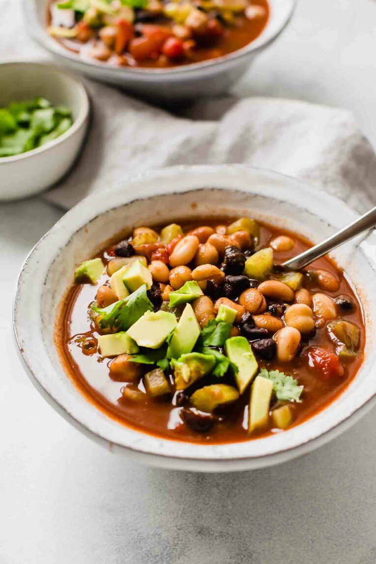 Angle shot of vegan chili with avocado in a white bowl.