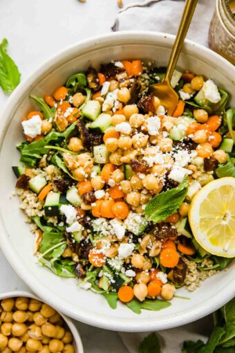 A top shot of a large bowl of carrot chickpea salad with feta cheese and a slice of lemon and mint leaves.