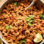 Spanish rice and red beans in a pan with cilantro and lime.