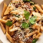 Parmesan sun-dried tomato chicken pasta in a white bowl with a fork.