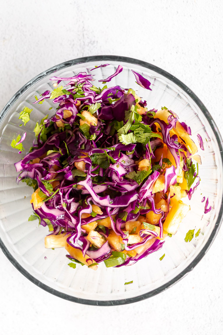 Cabbage pineapple slaw being mixed in a bowl.