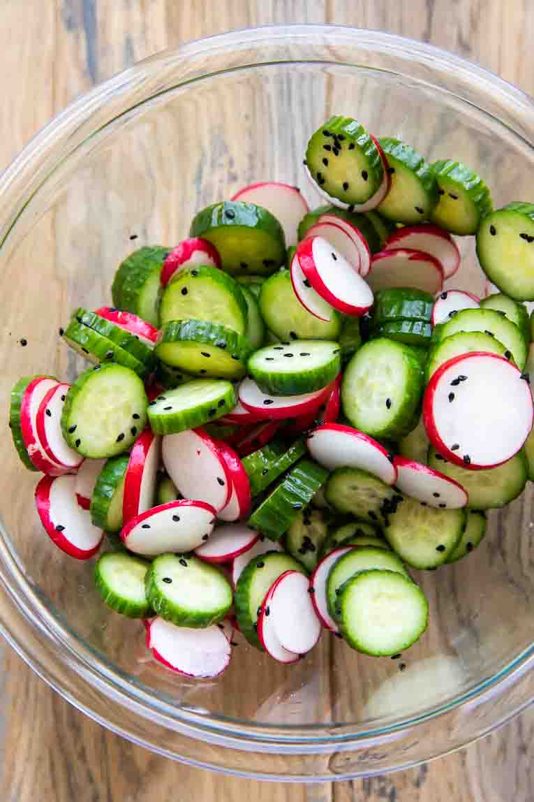 Radishes and cucumbers in a mixing bowl being marinated.