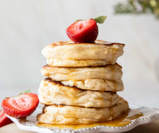 A stack of Souffle Pancakes on a plate topped with a strawberry.