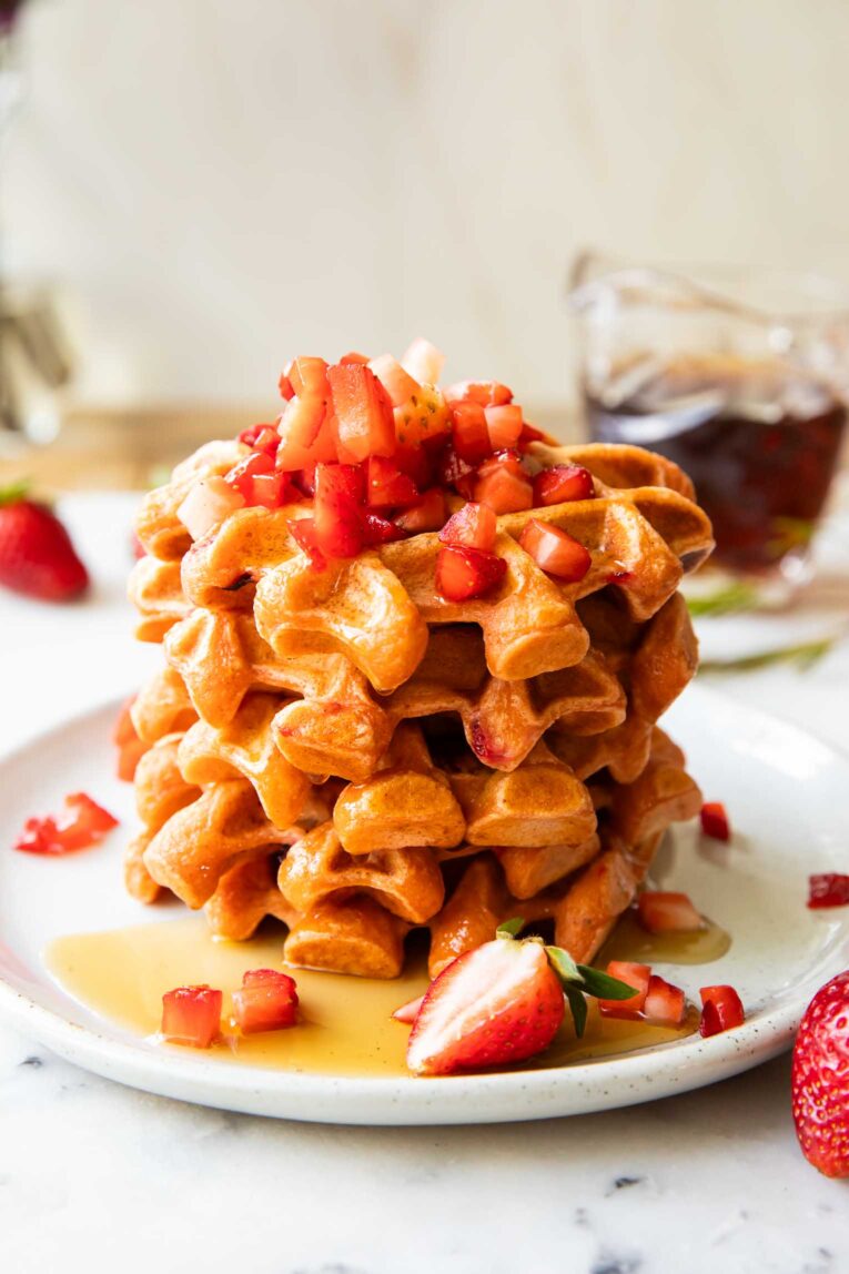 Angled image of a stack of waffles on a plate with maple syrup.
