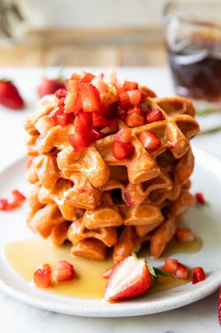 Angled image of a stack of waffles on a plate with maple syrup.