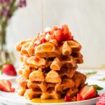 A stack of waffles on a plate with maple syrup.