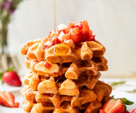 A stack of waffles on a plate with maple syrup.