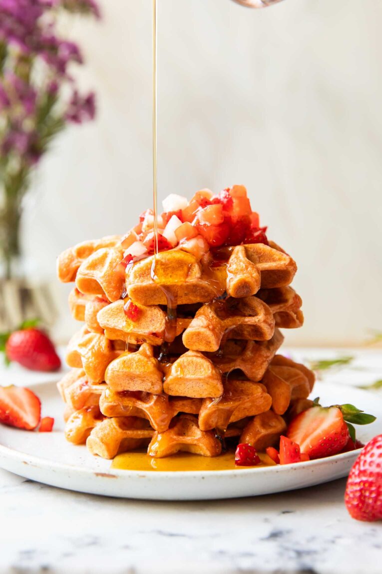 A stack of waffles on a plate with maple syrup.